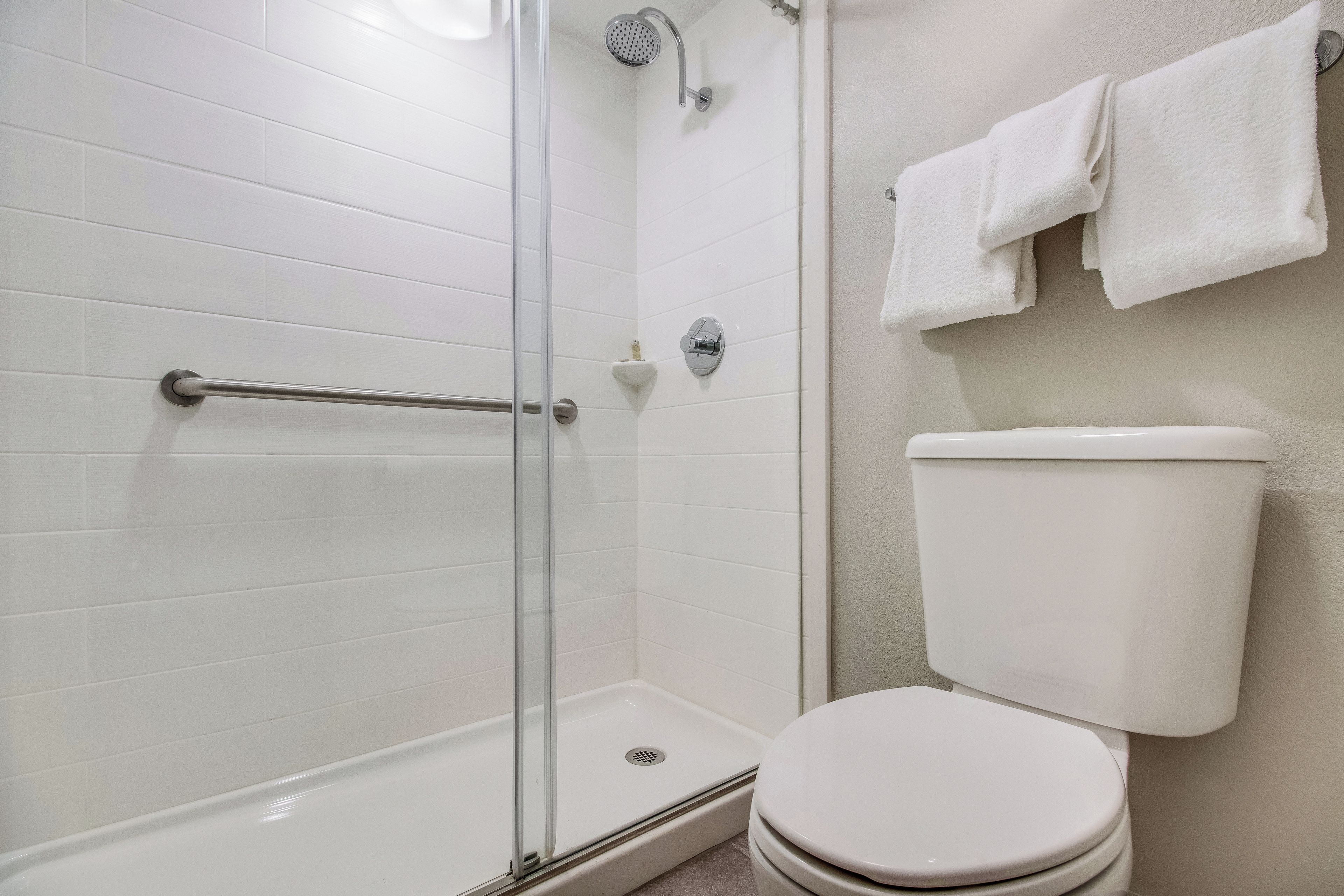 Un baño con ducha de vidrio, inodoro blanco y toallero con dos toallas.