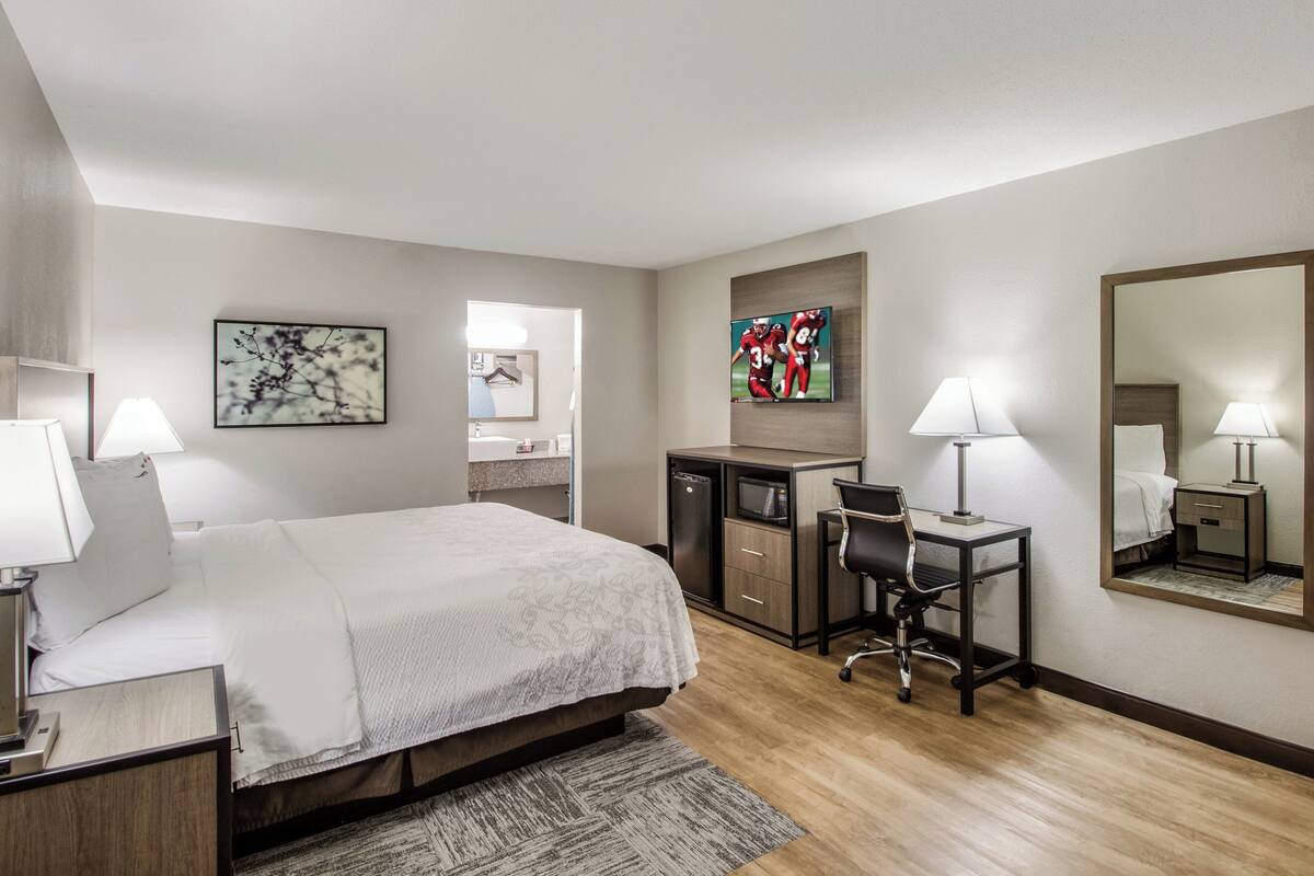 A hotel room with a bed, desk, chair, and a large mirror.