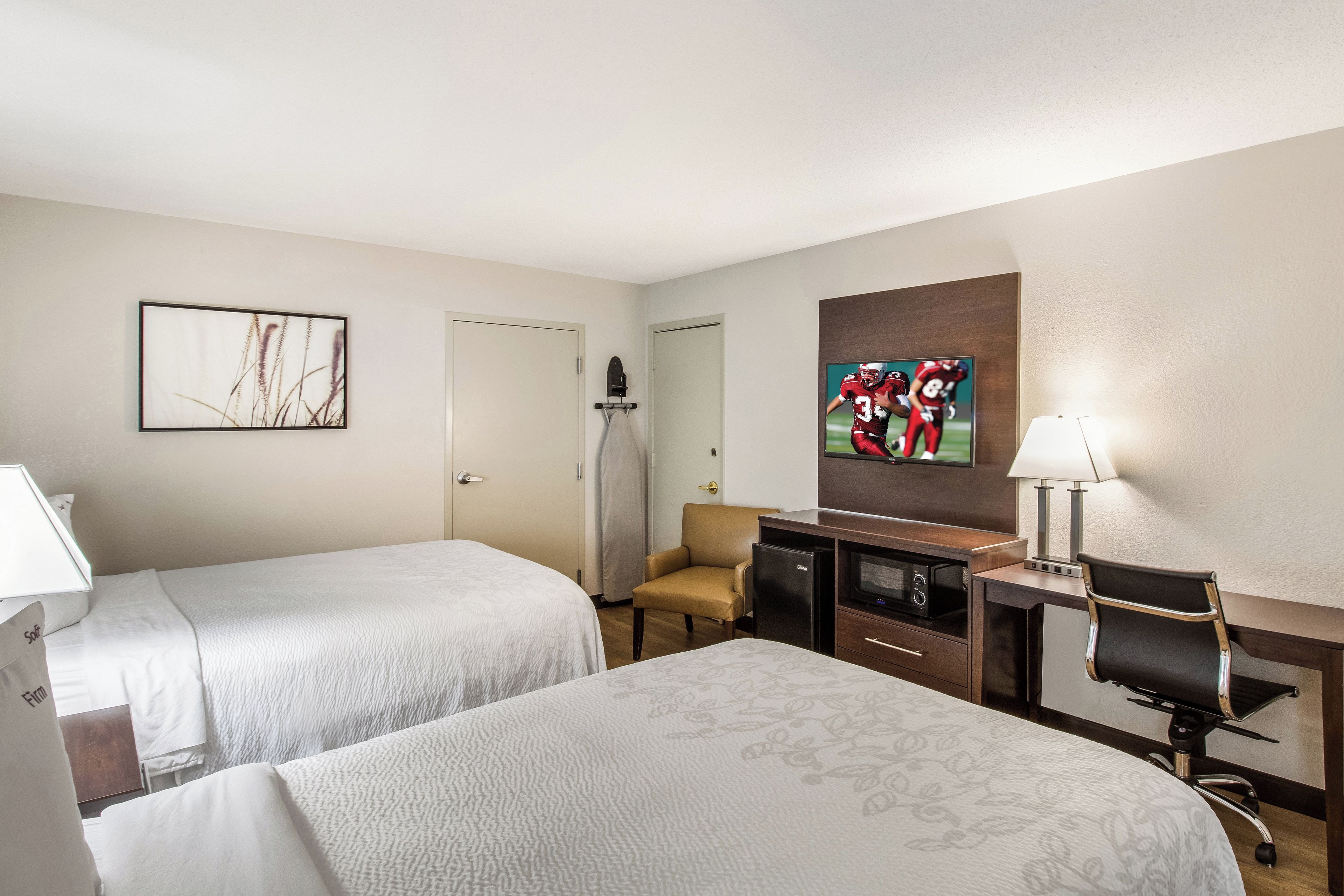 A hotel room with two beds, a desk with a television, a chair, and a small refrigerator.
