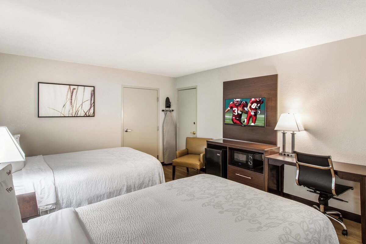 A hotel room with two beds, a desk with a television, a chair, and a small refrigerator.