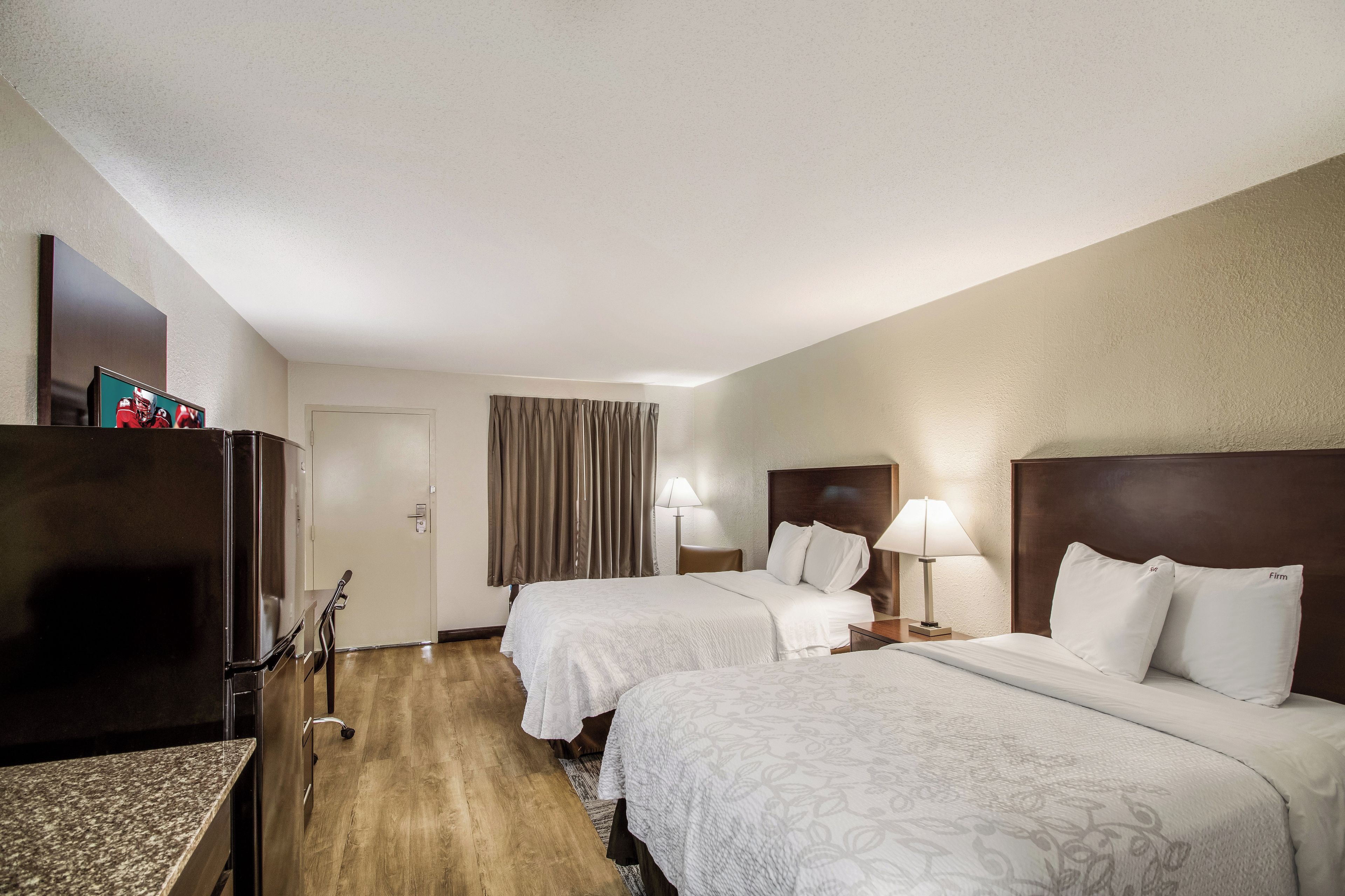 Habitación de hotel con dos camas, un escritorio, un televisor y una puerta.