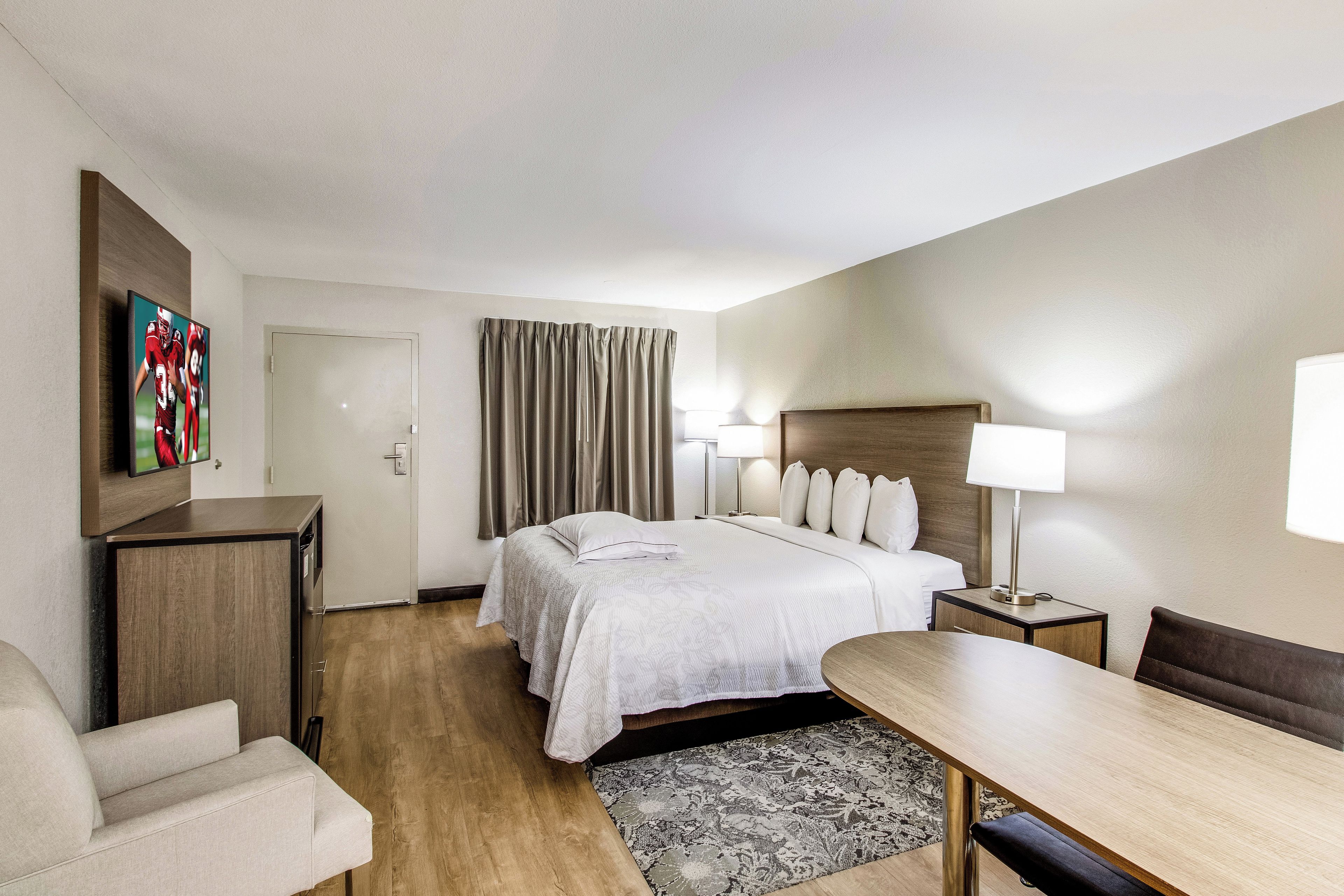 Habitación de hotel con cama, mesitas de noche, escritorio, silla, televisor y puerta.