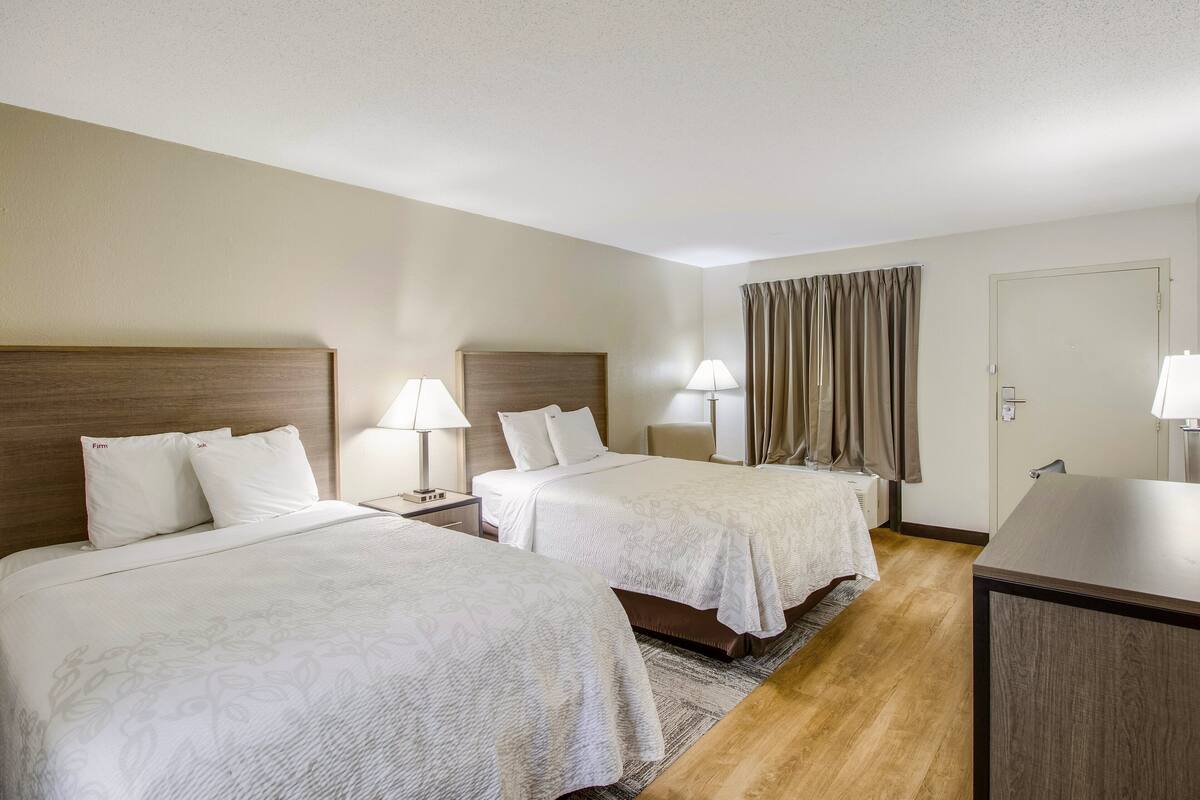 A hotel room with two beds, a desk, and a window with curtains.