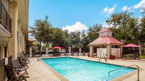 A swimming pool with lounge chairs and umbrellas, surrounded by trees and a building with a red roof.