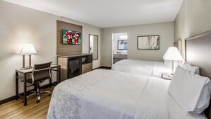 A hotel room with two beds, a desk, a chair, a TV, and a bathroom visible through an open door.