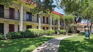 A multi-story hotel with a brick facade, balconies, and a well-maintained lawn. - Red Roof Inn PLUS+ Dallas – Addison (Addison)