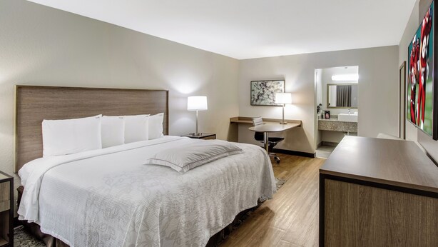 A hotel room with a large bed, bedside lamps, a desk with a chair, a mirror, and a wall-mounted TV.