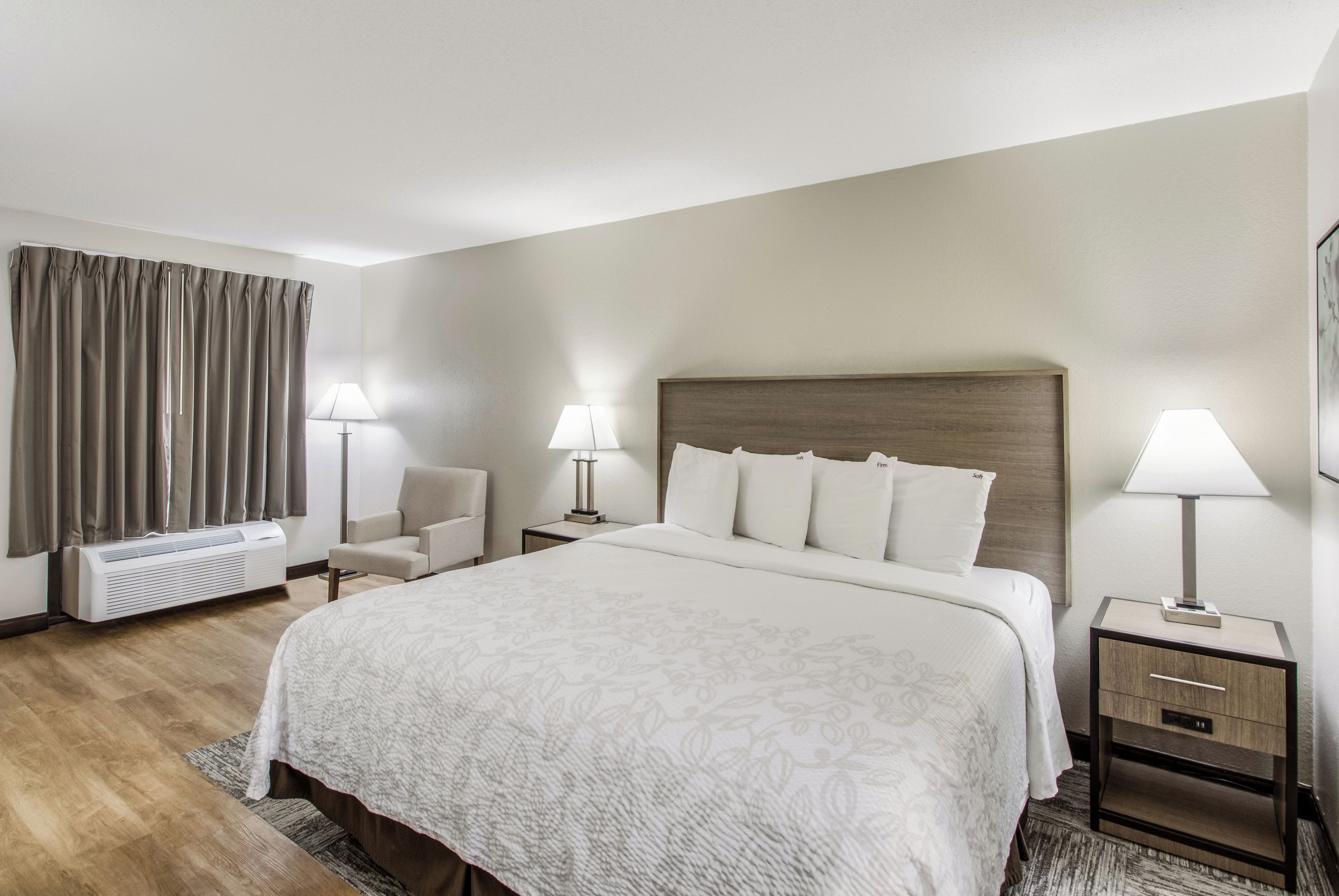 Habitación de hotel con una cama grande, dos mesitas de noche con lámparas, una silla, un escritorio, una lámpara de escritorio y una ventana con cortinas.