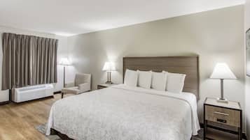 Habitación de hotel con una cama grande, dos mesitas de noche con lámparas, una silla, un escritorio, una lámpara de escritorio y una ventana con cortinas.