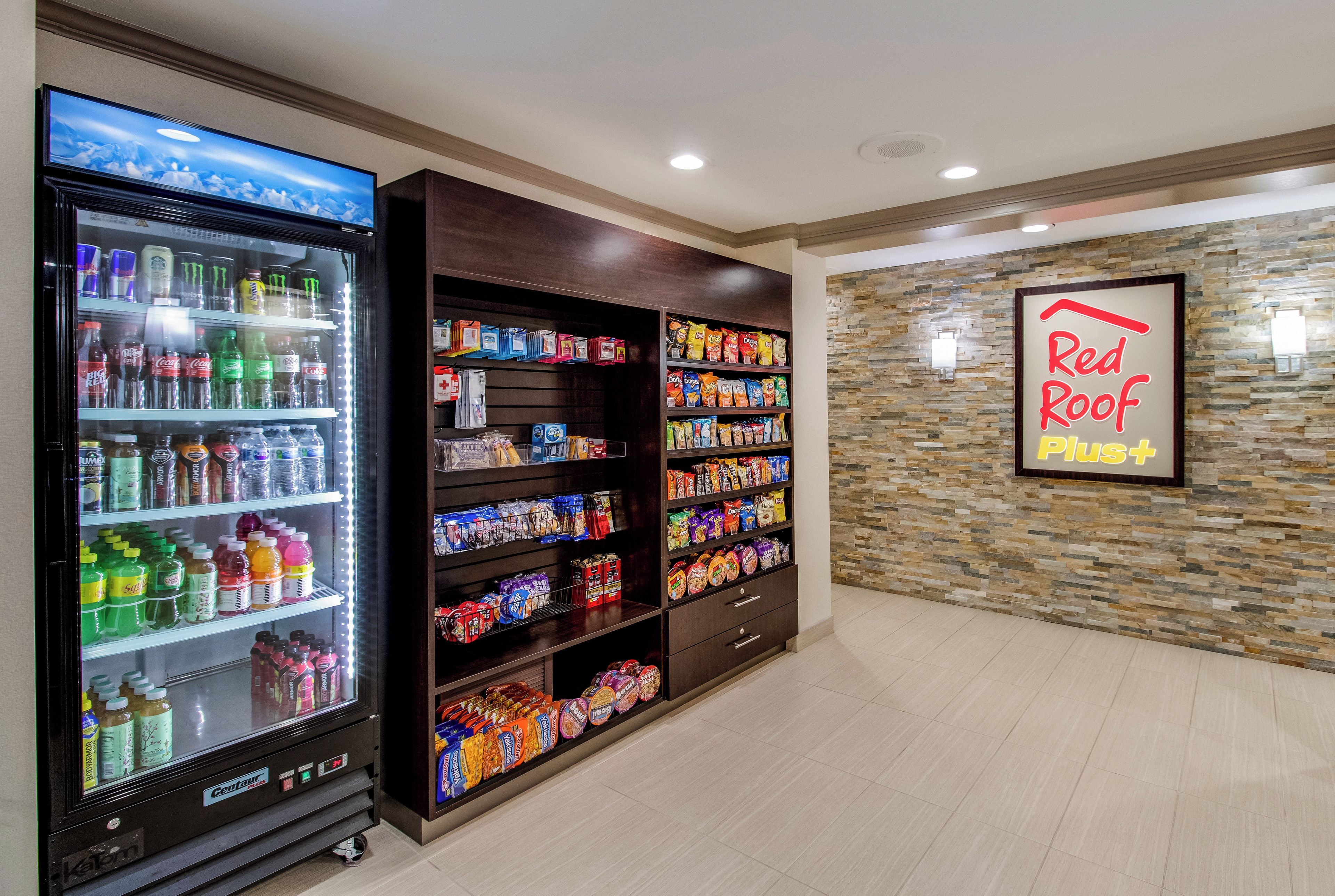 Máquina expendedora llena de bebidas y aperitivos, una pared con el letrero 'Red Roof Plus' y una pared con textura de piedra.
