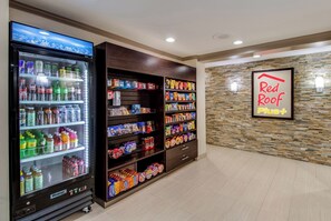 A vending machine stocked with beverages and snacks, a wall with a 'Red Roof Plus' sign, and a stone-textured wall. - Red Roof Inn PLUS+ Dallas – Addison (Addison)