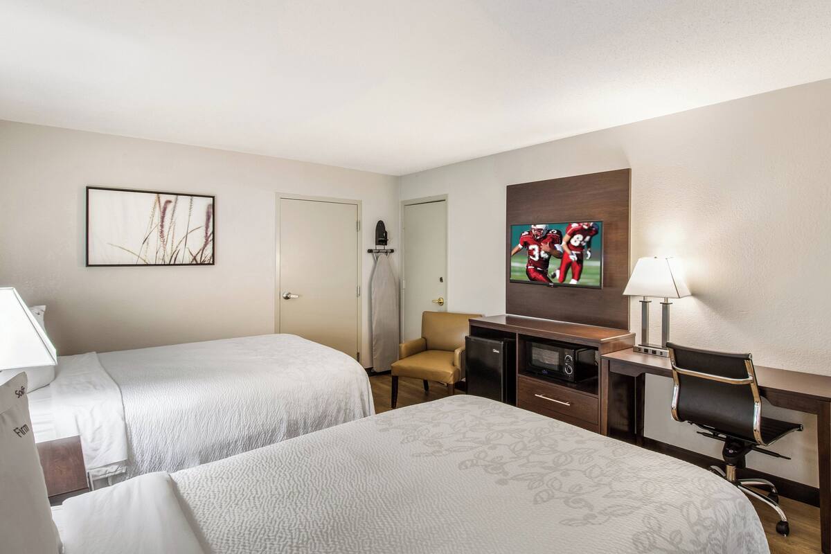 A hotel room with two beds, a desk with a lamp, a TV, and a chair.