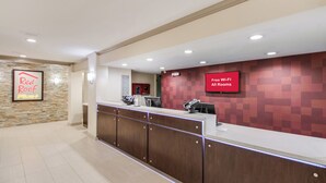 Zona de recepción de un hotel con pared de piedra, un cartel de Red Roof Plus, un aviso de Wi-Fi gratuito y un mostrador de recepción.