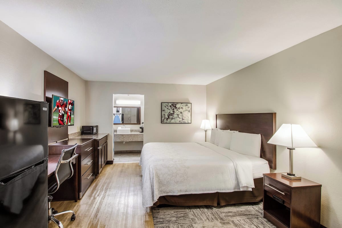 A hotel room with a bed, bedside table, lamp, desk, chair, TV, and artwork on the walls.