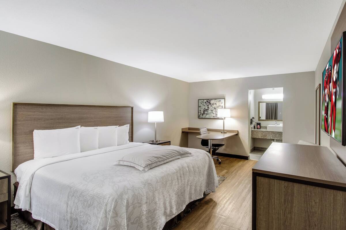 A hotel room with a large bed, bedside tables, a desk, a chair, a desk lamp, a mirror, and a framed picture on the wall.