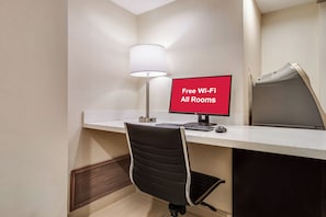 Habitación de hotel con escritorio, una silla, computadora, lámpara y un letrero que indica acceso a Wi-Fi gratuito.