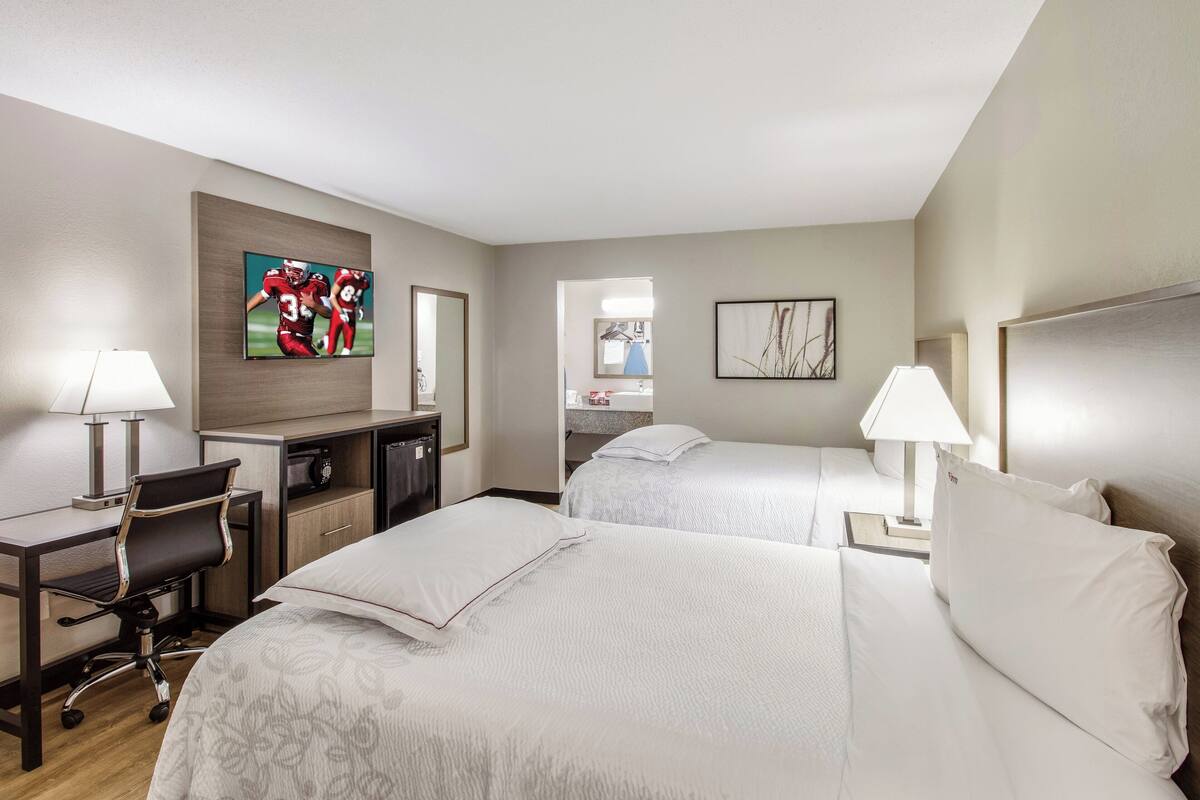 A hotel room with two beds, a desk, a chair, a TV, and a mirror.