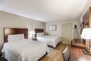 A hotel room with two beds, a desk, a chair, a lamp, and a door. - Red Roof Inn PLUS+ Dallas – Addison (Addison)