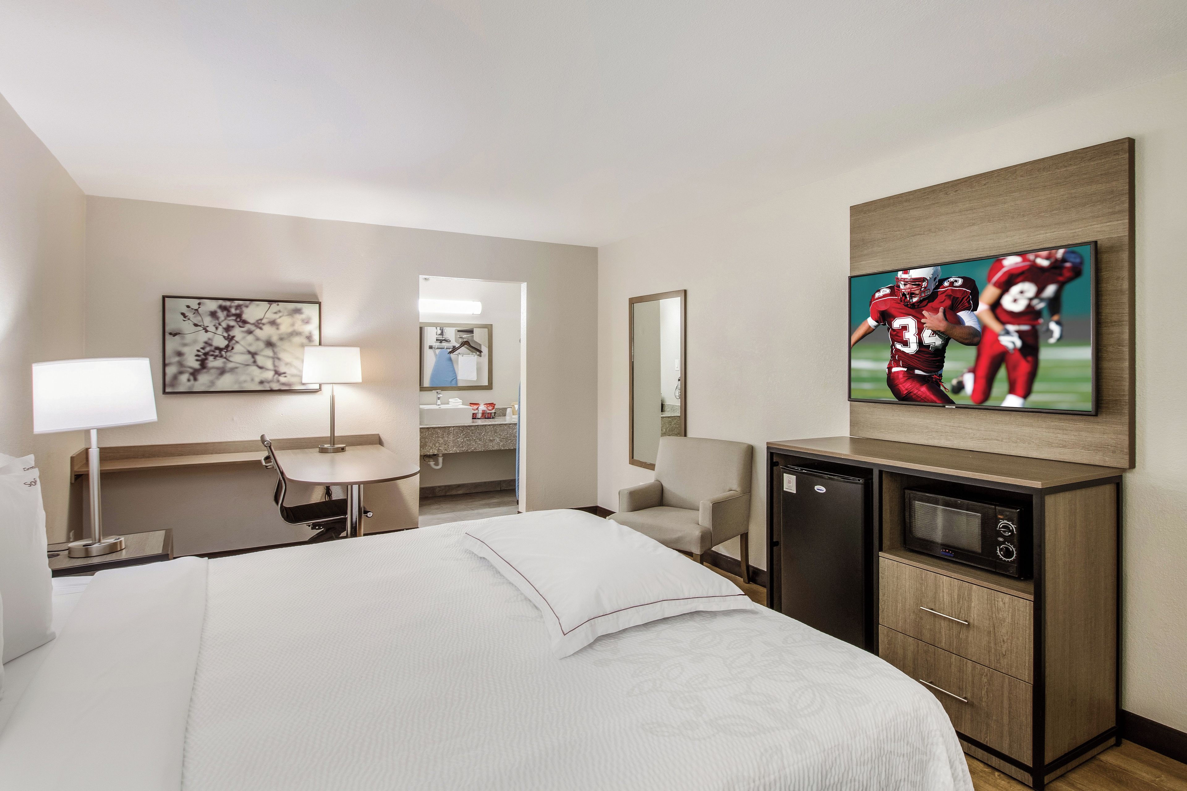 Habitación de hotel con cama, escritorio, silla, televisor y microondas.