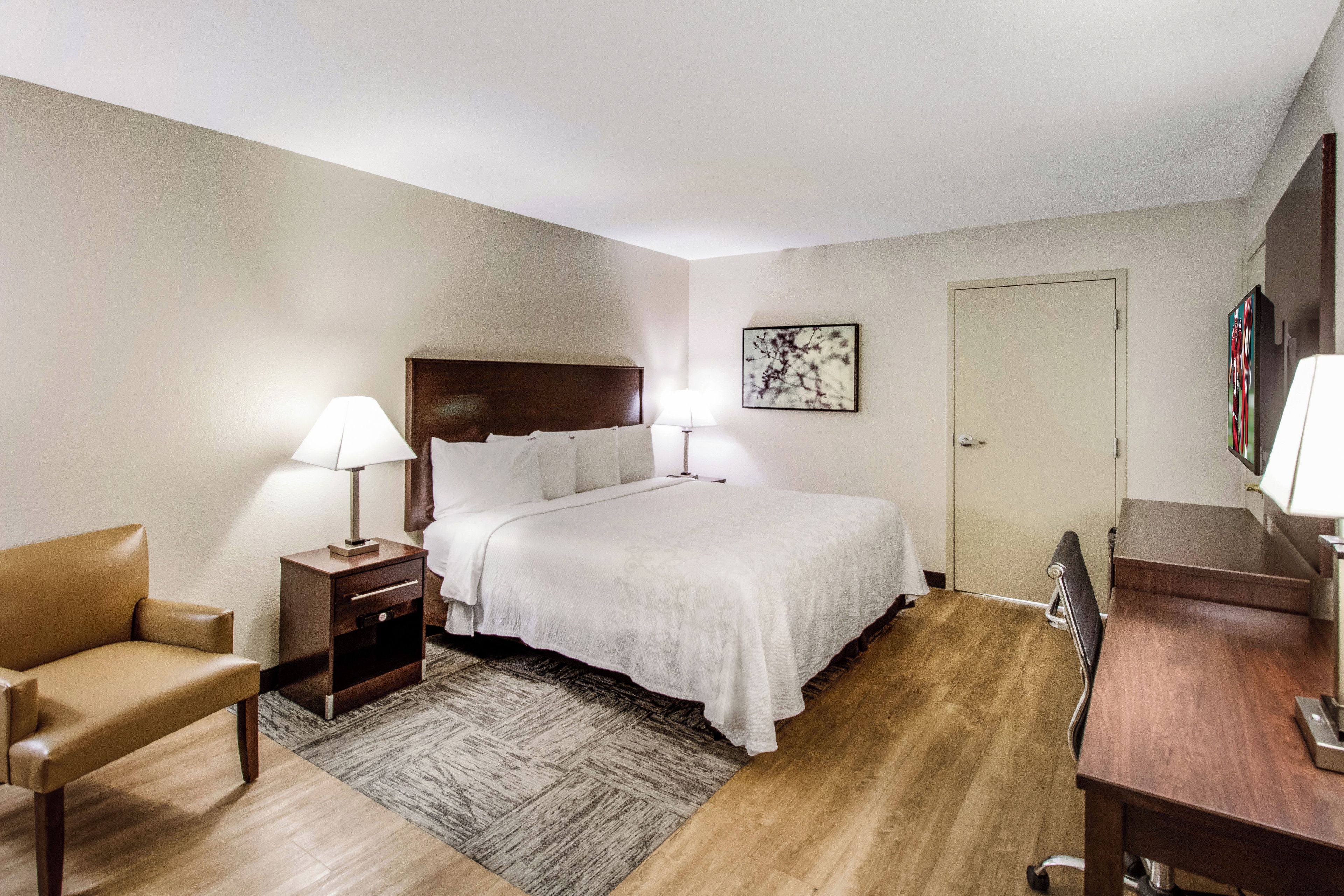 A hotel room with a bed, bedside tables, a chair, a desk, and a door.