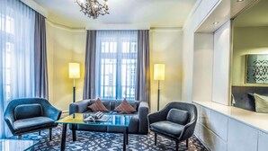 Una camera d'albergo moderna con divano, due poltrone, un tavolino in vetro e una tappeto decorato.