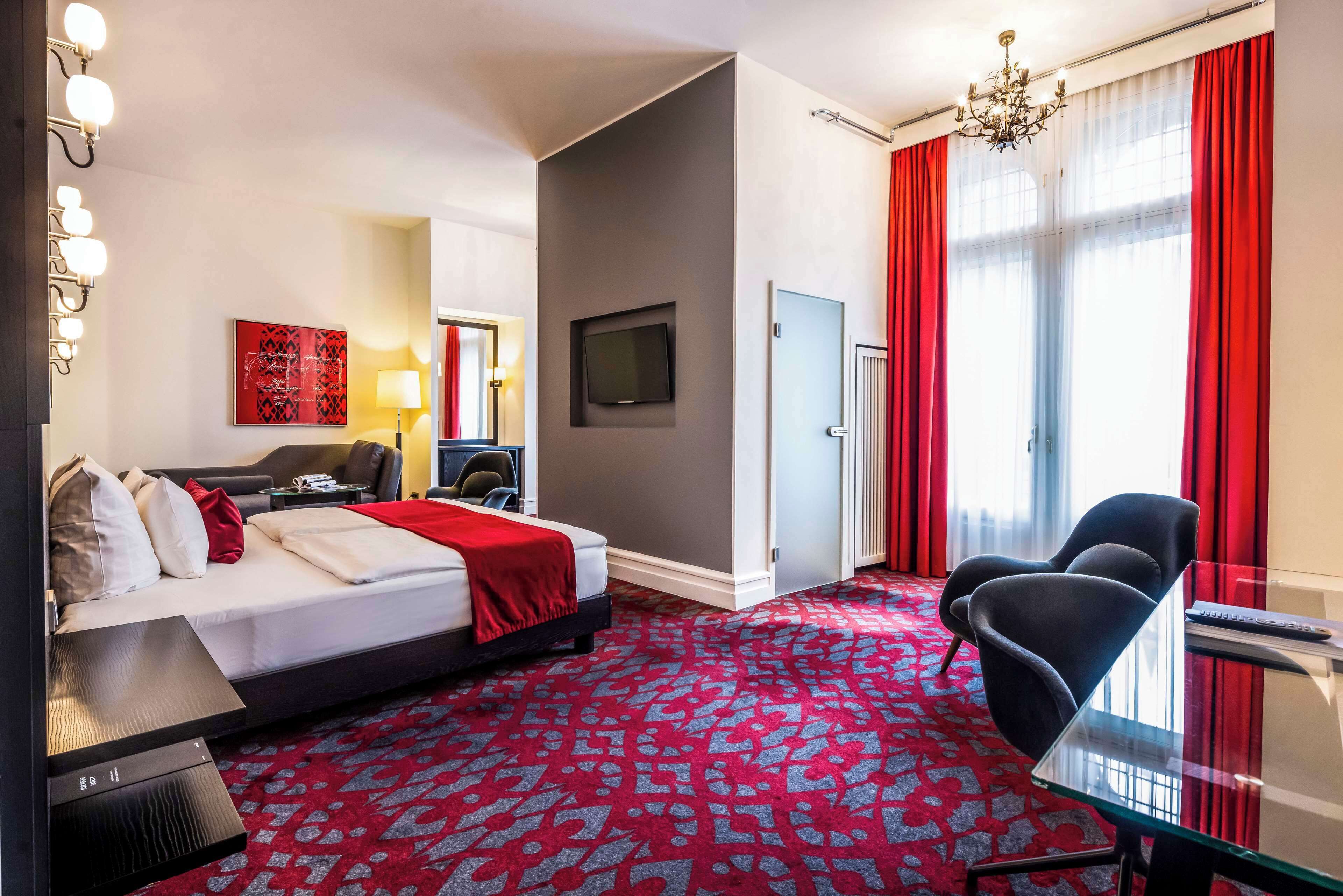 A hotel room with a bed, a desk, a chair, a TV, and a red carpet.