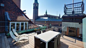 Una terrazza sul tetto con tavolo e sedie, con vista su un edificio storico con una torre dell'orologio.