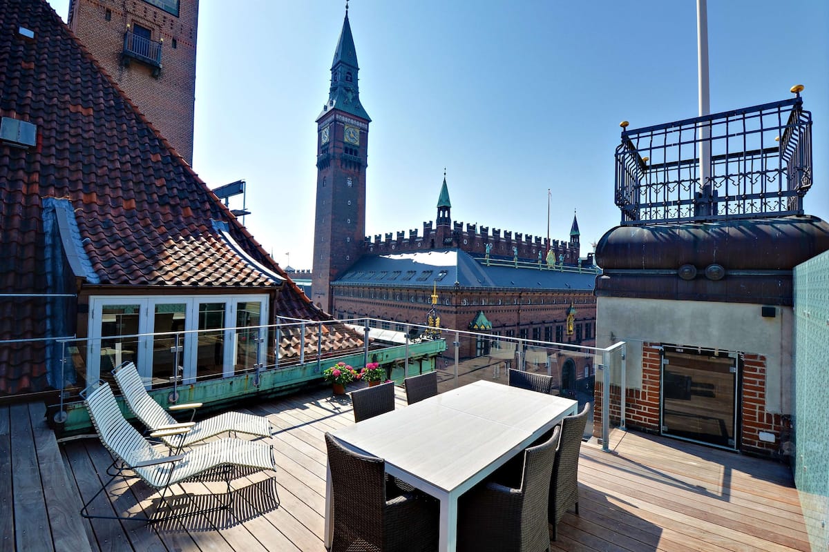 A rooftop terrace with a table and chairs, overlooking a historic building with a clock tower.
