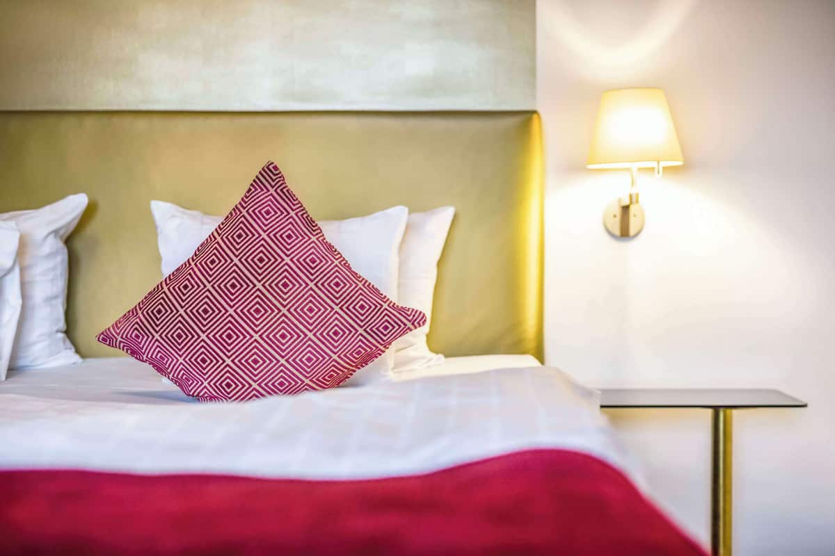 A neatly made bed with a patterned pillow, a bedside table, and a wall-mounted lamp.