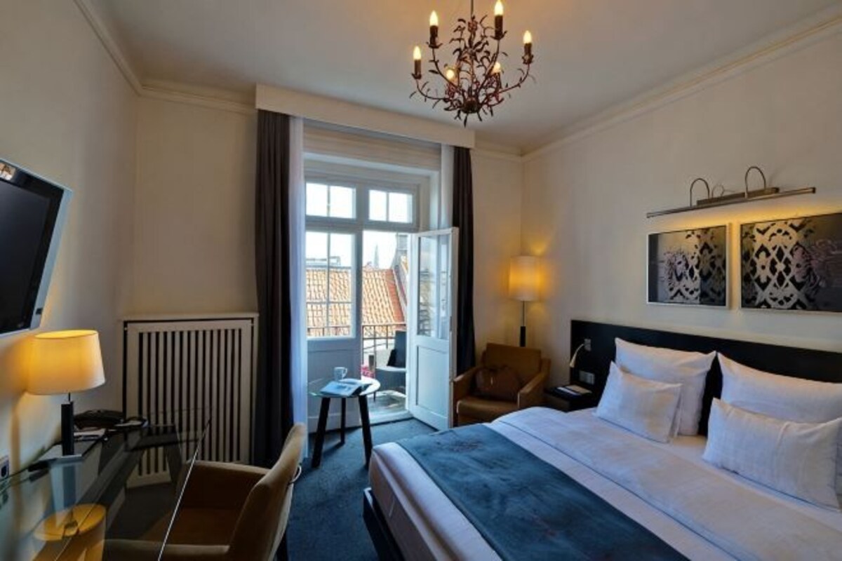 Una camera d'albergo con un letto, una scrivania, una sedia, una televisione e un lampadario.