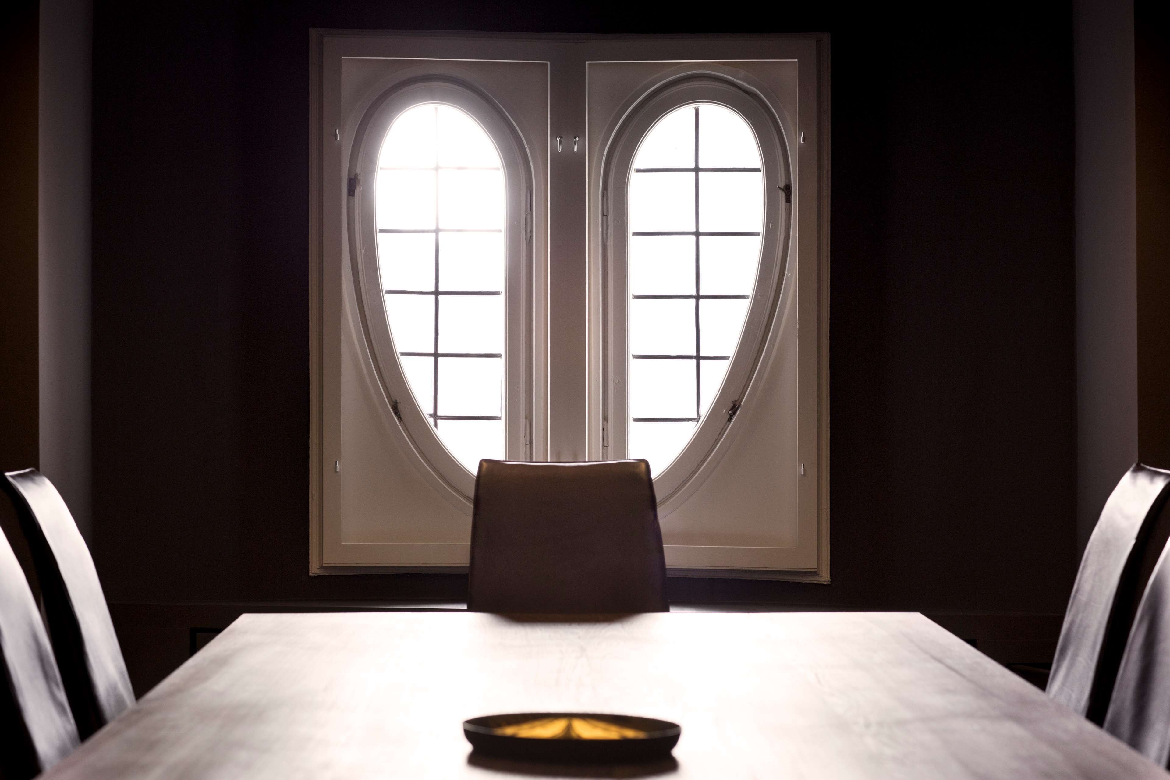 A dining area with a table and chairs, a window with a grid pattern, and a light source on the table.