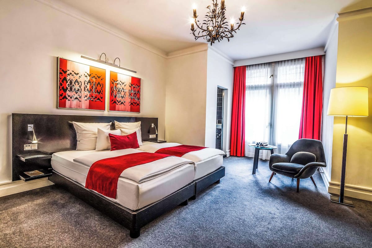 A hotel room with a large bed, a desk, a chair, and a chandelier.