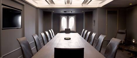 Un salón de conferencias con una mesa larga, sillas, una televisión y un ventanal de dos cristales.