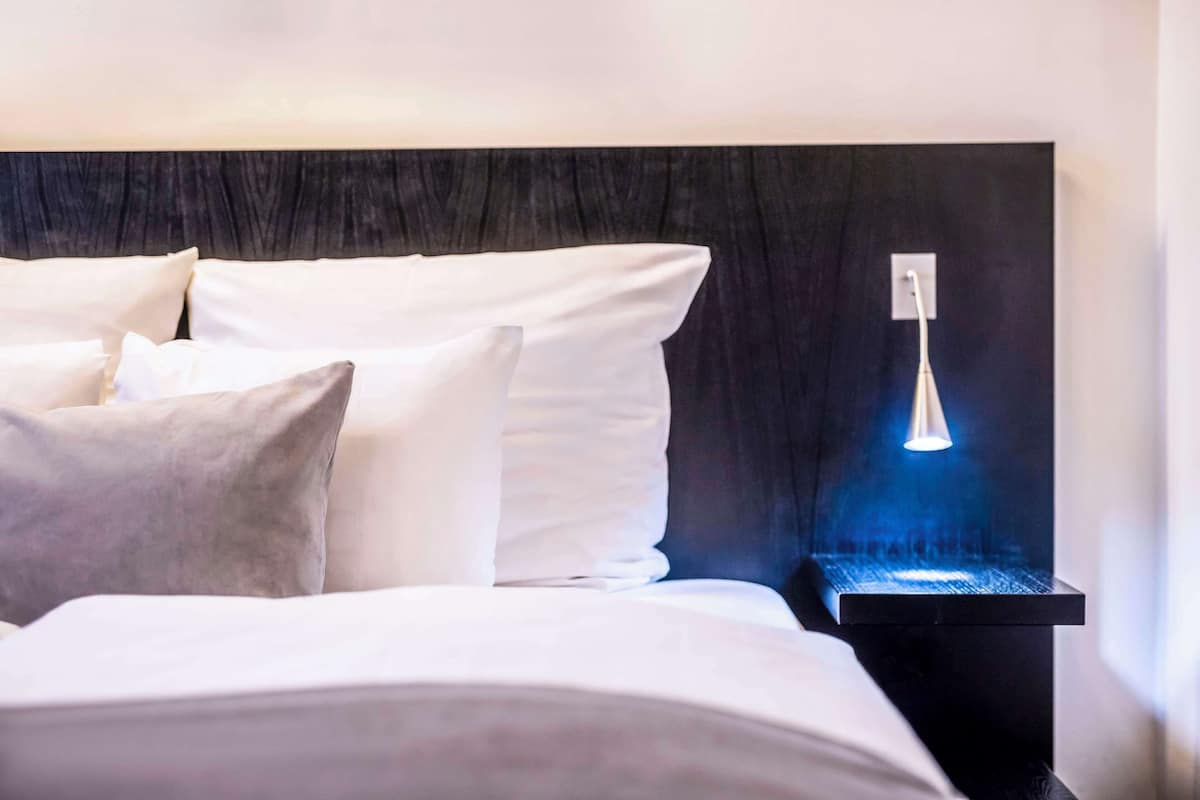 A neatly made bed with white linens and pillows, a black headboard, and a bedside table with a blue-lit lamp.