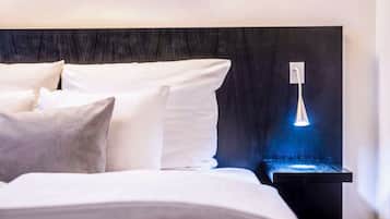 A neatly made bed with white linens and pillows, a black headboard, and a bedside table with a blue-lit lamp.