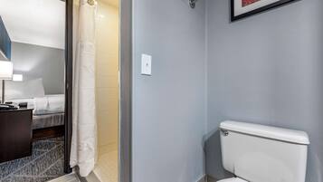 A bathroom with a toilet, a shower curtain, a bed, and a bedside table.