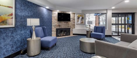 A modern hotel lobby with a stone wall, a flat-screen TV, a fireplace, and comfortable seating areas.