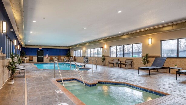 Una piscina interior con suelo de baldosas, sillas de descanso y una puerta al fondo.