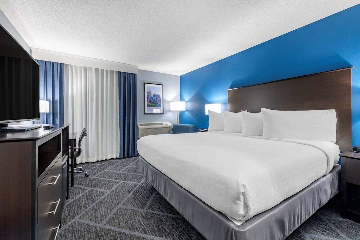 A hotel room with a large bed, a desk with a computer, a chair, and a lamp.