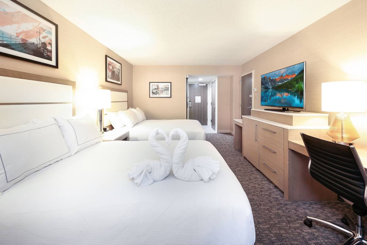 Quarto de hotel com duas camas, uma escrivaninha, uma cadeira e uma televisão.