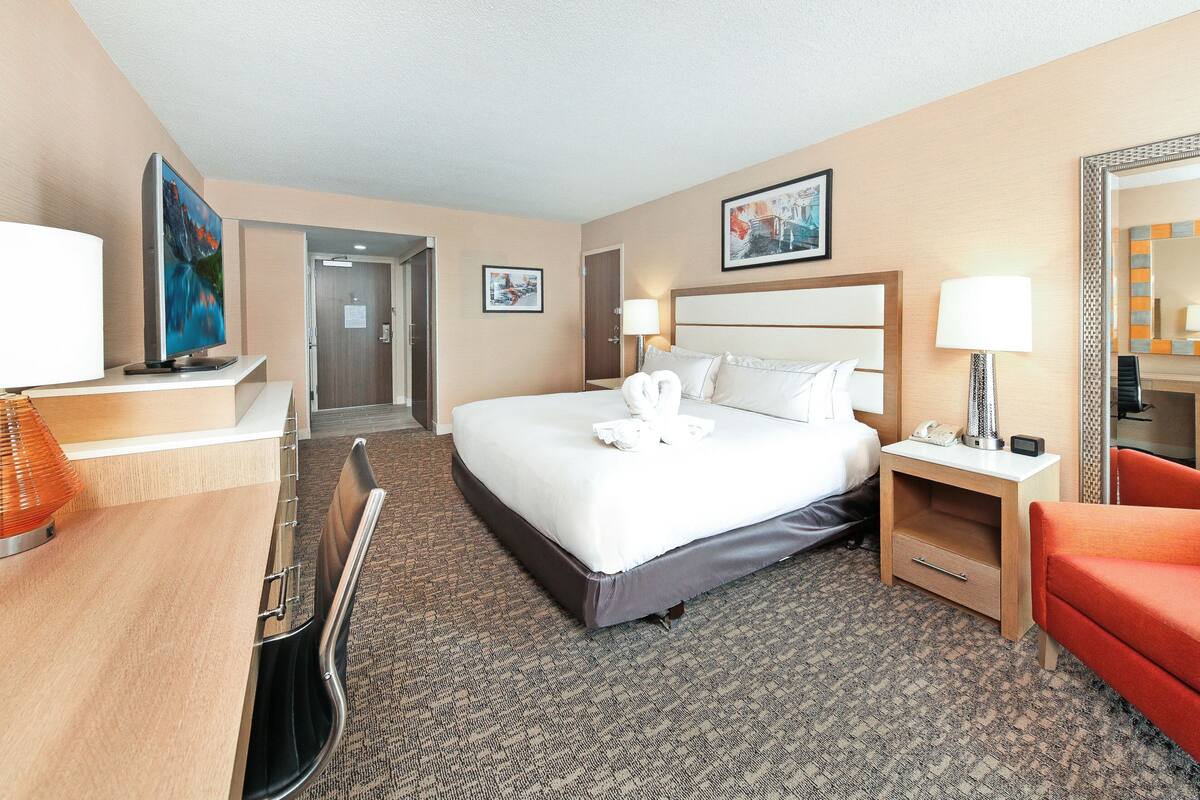 Quarto de hotel com cama, escrivaninha, cadeira, abajur e espelho.