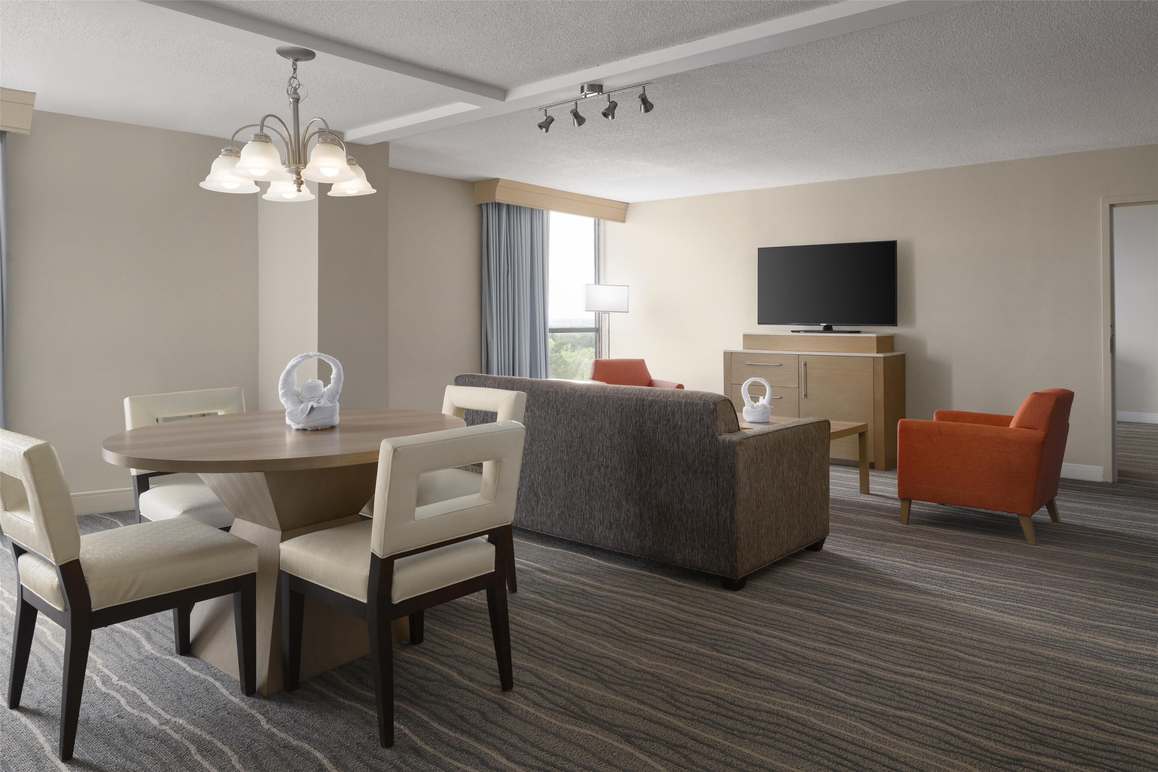A hotel room with a dining table, chairs, a sofa, a TV, and a carpeted floor.