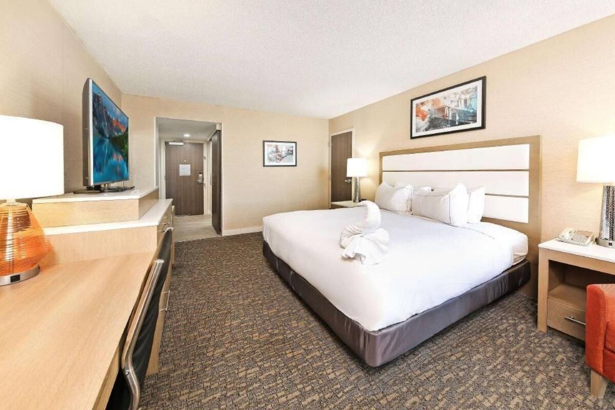 Quarto de hotel com cama, mesas de cabeceira, escrivaninha, cadeira, televisão e obras de arte nas paredes.