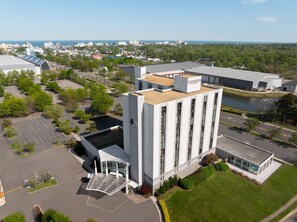 A modern building with a large parking lot, a covered entrance, and a view of the surrounding cityscape and water. - DoubleTree by Hilton Virginia Beach (Virginia Beach)
