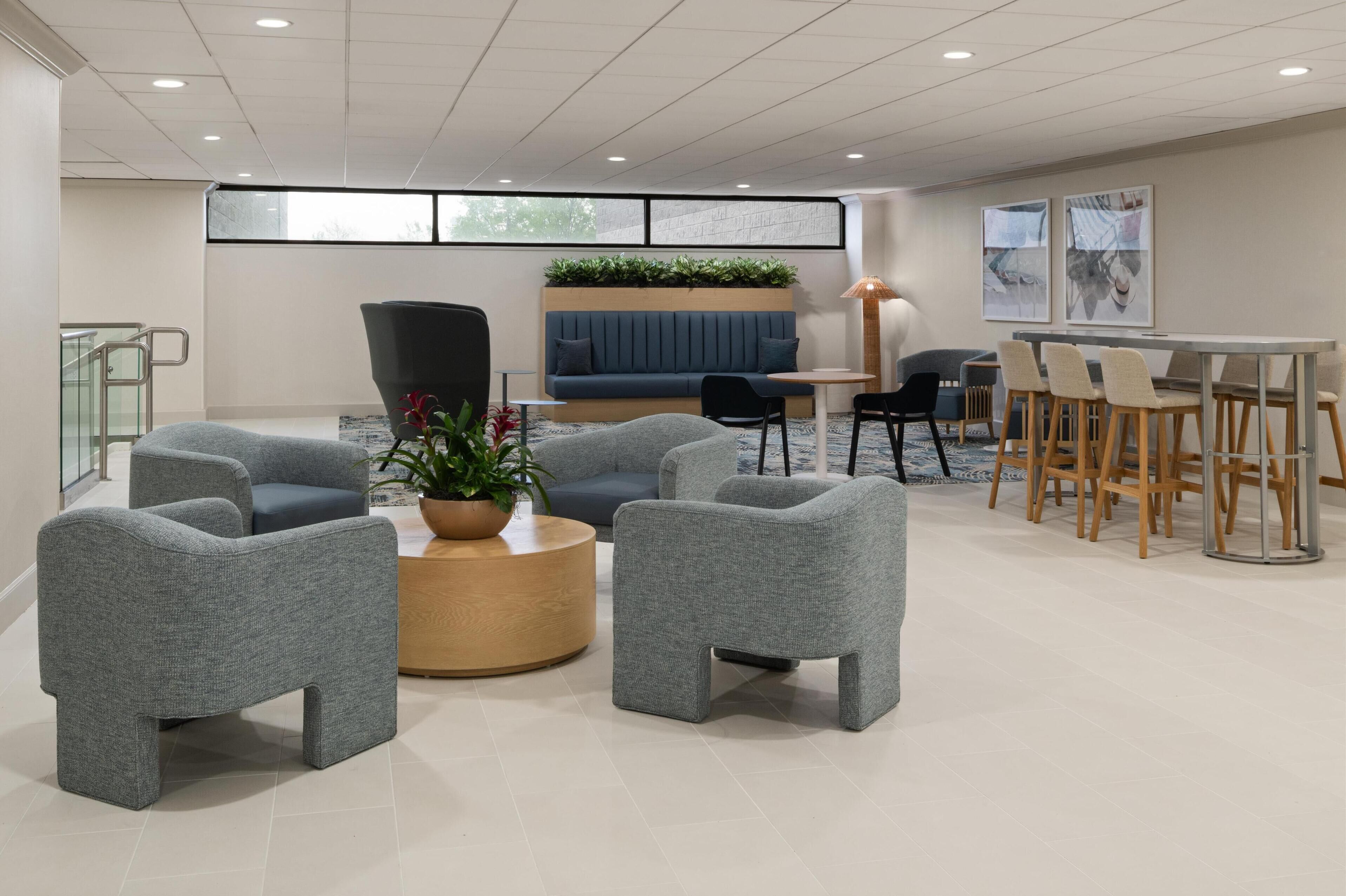 A modern lounge area with grey upholstered chairs, a round wooden coffee table, a blue sofa, and a dining table with chairs.