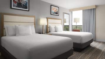 A hotel room with two beds, a large window with curtains, and two framed pictures on the wall.