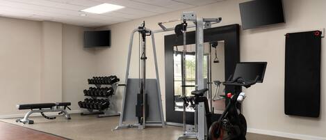 Une salle de sport équipée de matériel d’exercice, d’un banc, d’haltères et d’un téléviseur fixé au mur.