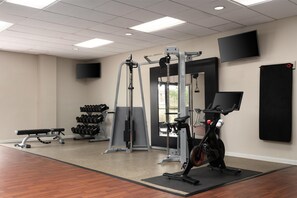 A gym with exercise equipment, a bench, dumbbells, and a TV on the wall. - DoubleTree by Hilton Virginia Beach (Virginia Beach)