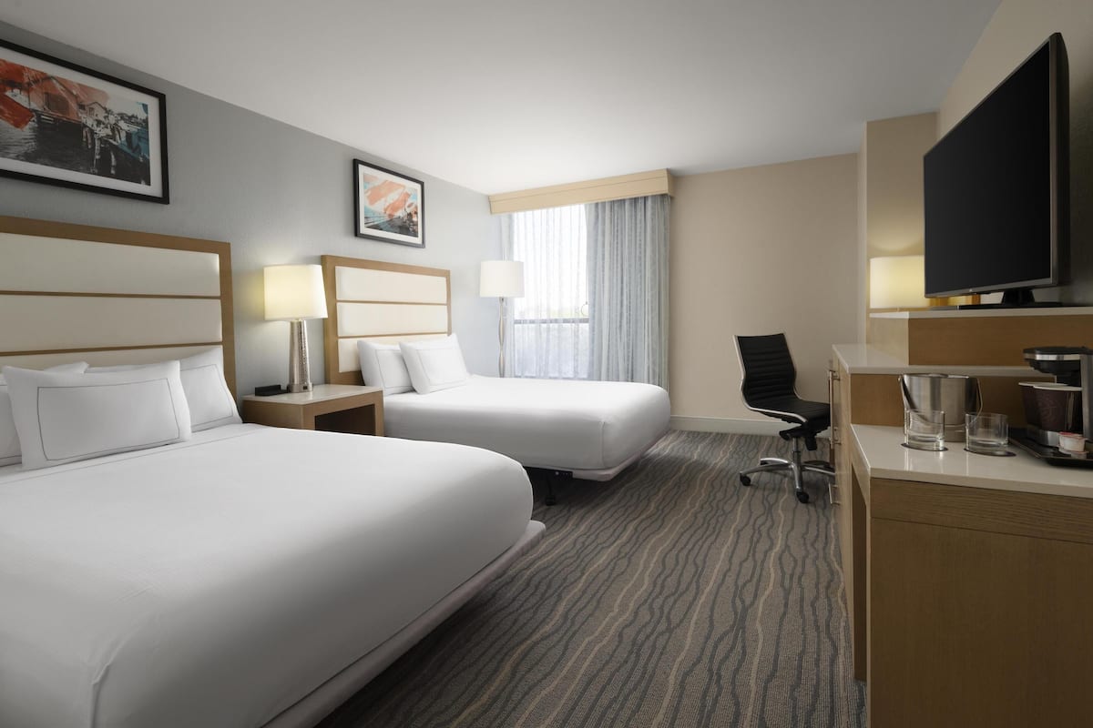 Quarto de hotel com duas camas, uma escrivaninha, uma televisão e uma janela com cortinas.