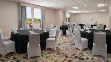 A conference room with round tables, white chairs, and black tablecloths.